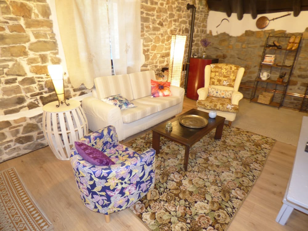 Turismo rural en La Viliella.Salón amplio del apartamento Luna Creciente en Casa Luna turismo rural en la Reserva de Muniellos. Salón del apartamento Luna Creciente en Casa Luna, La Viliella, Asturias, con suelos de madera, paredes de piedra, techos abuhardillados de madera, sofá, sillones, chimenea y gran ventanal.